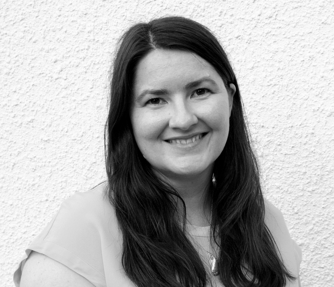 A black and white photo of a woman smiling warmly with long dark hair against a plain background.